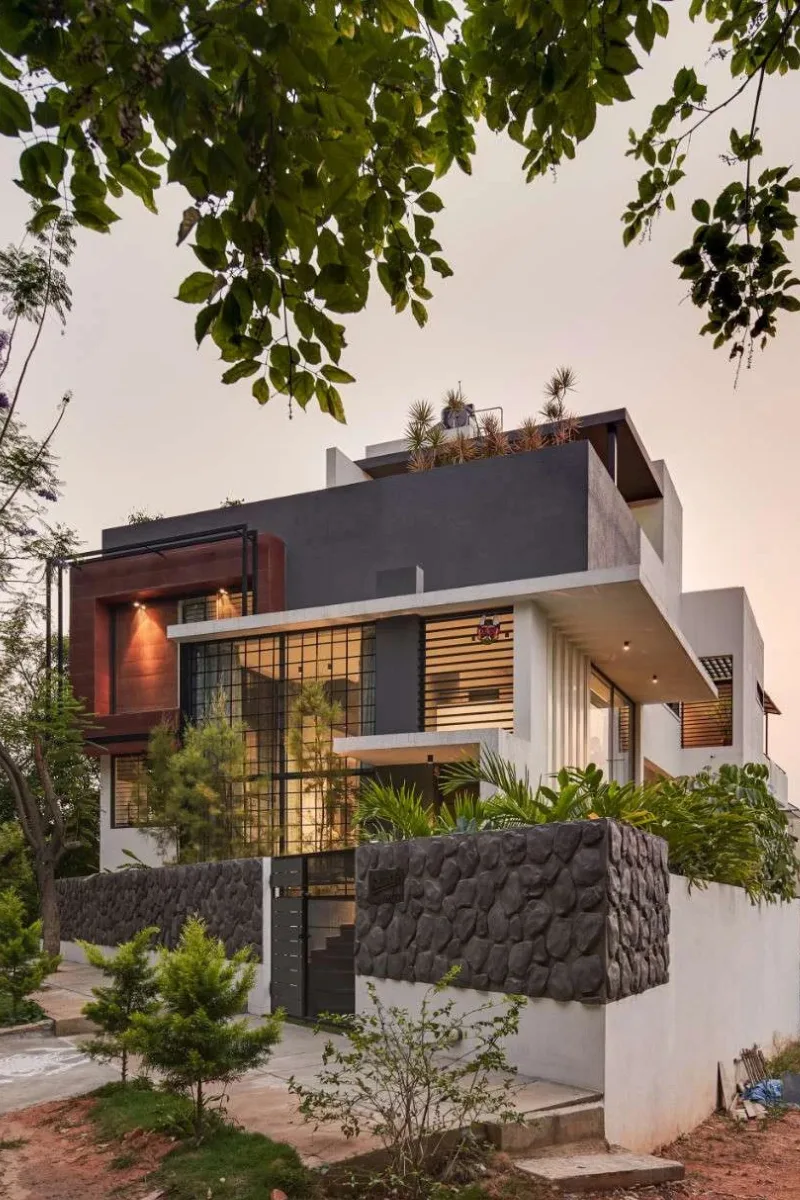 Contemporary multi-story house with double-height grid glass window and stone compound wall designed by architects in Bangalore