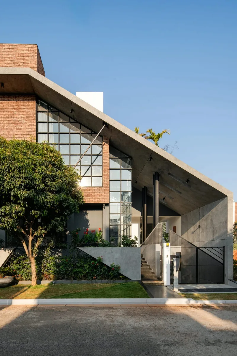 Vertical view of a modern house featuring a sloped concrete canopy and brick facade designed by architects in Bangalore