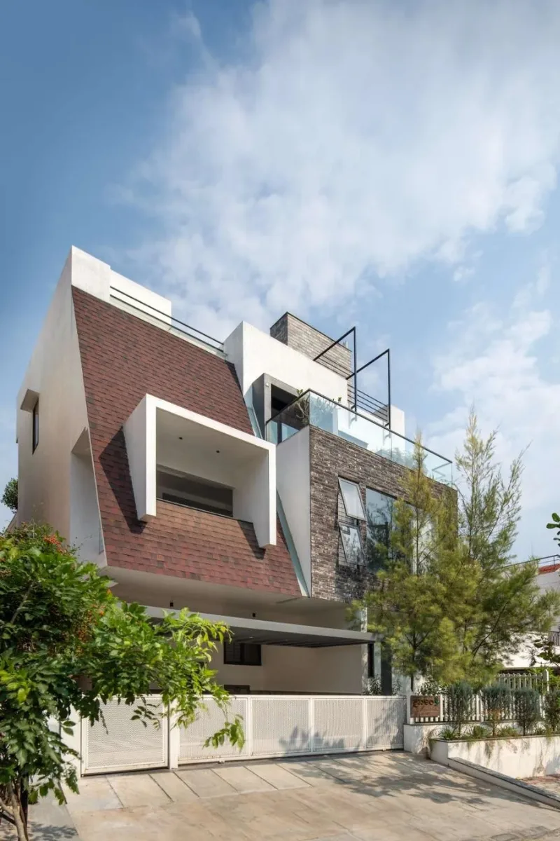 Modern multi-level home with reddish-brown pitched shingle roof and brick facade designed by architects in Bangalore