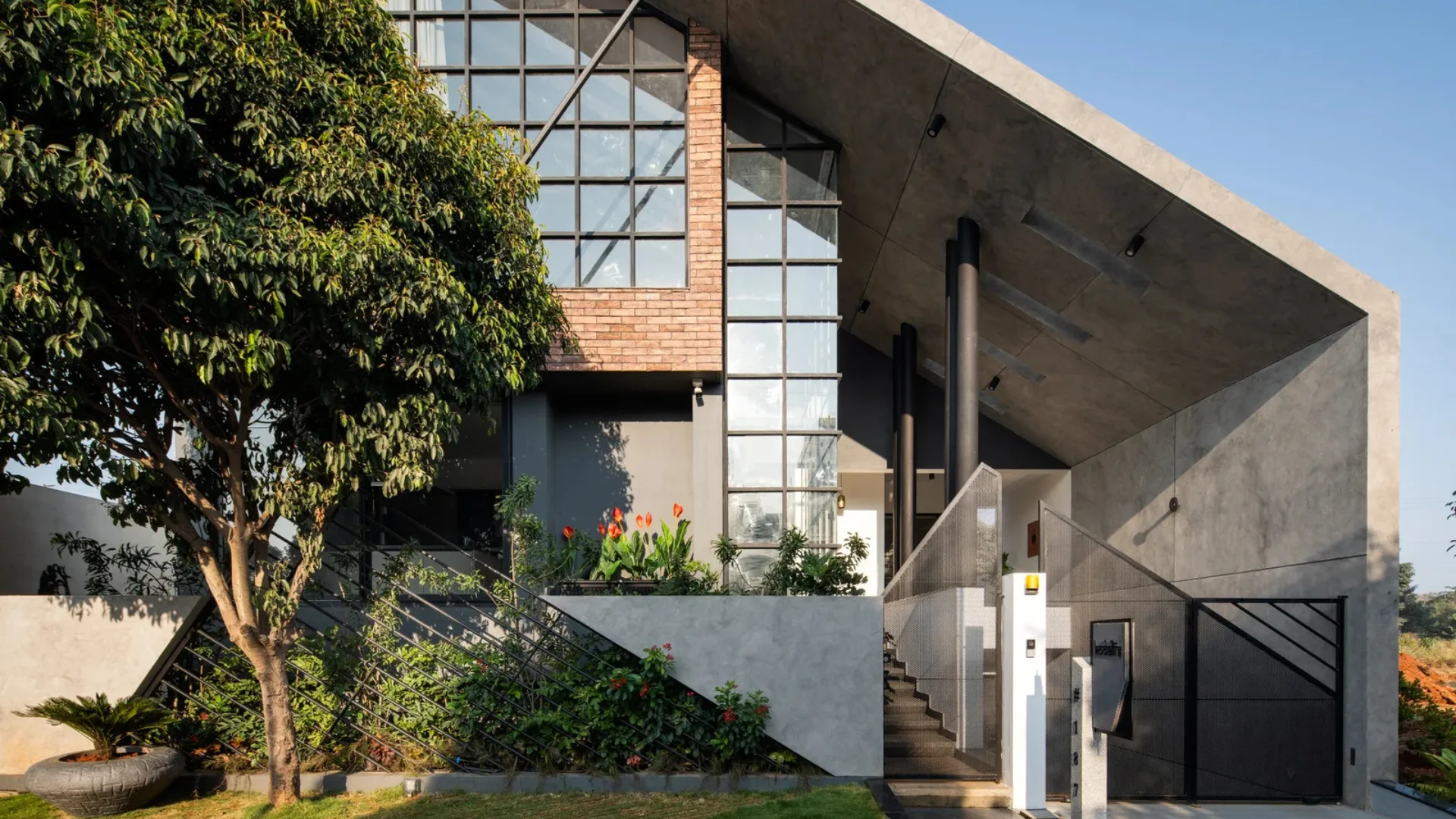 Contemporary industrial residence designed by architects in Bangalore featuring raw brick accents, black grid window wall, and sweeping concrete overhang