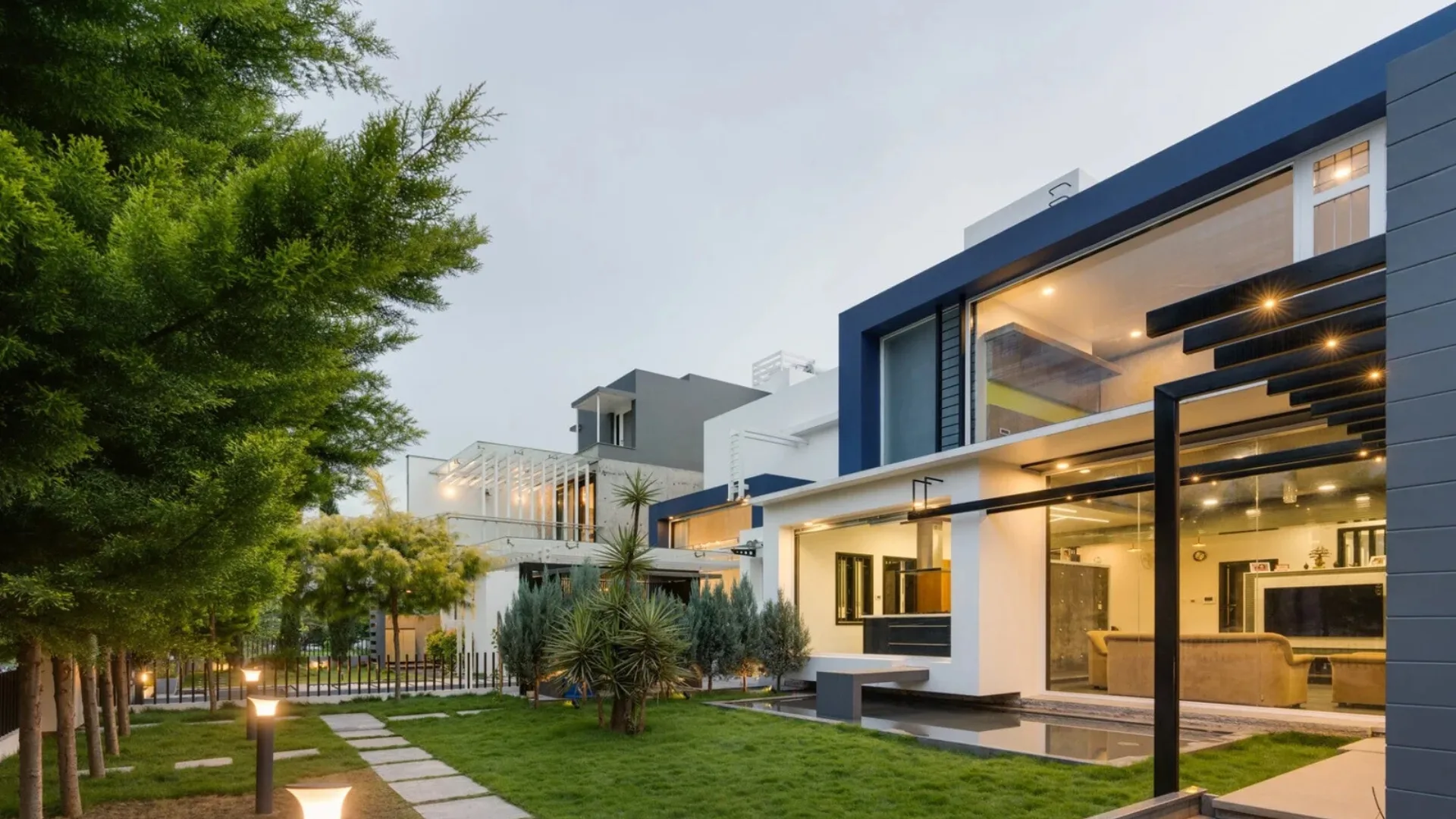 Contemporary two-story house with navy blue trim and floor-to-ceiling glass wall opening to a landscaped garden, designed by architects in Bangalore