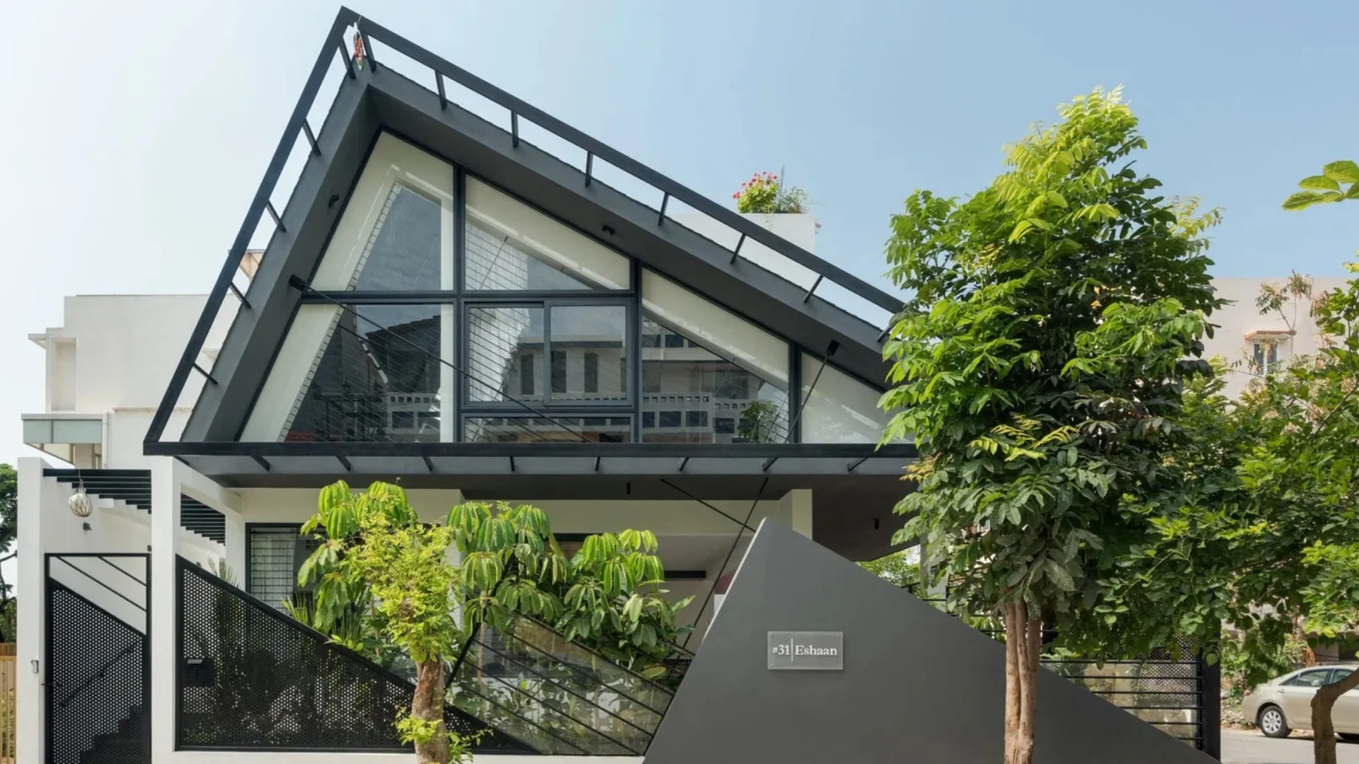 Modern bungalow elevation designed by architects in Bangalore featuring a triangular glass roof and dark metal frame