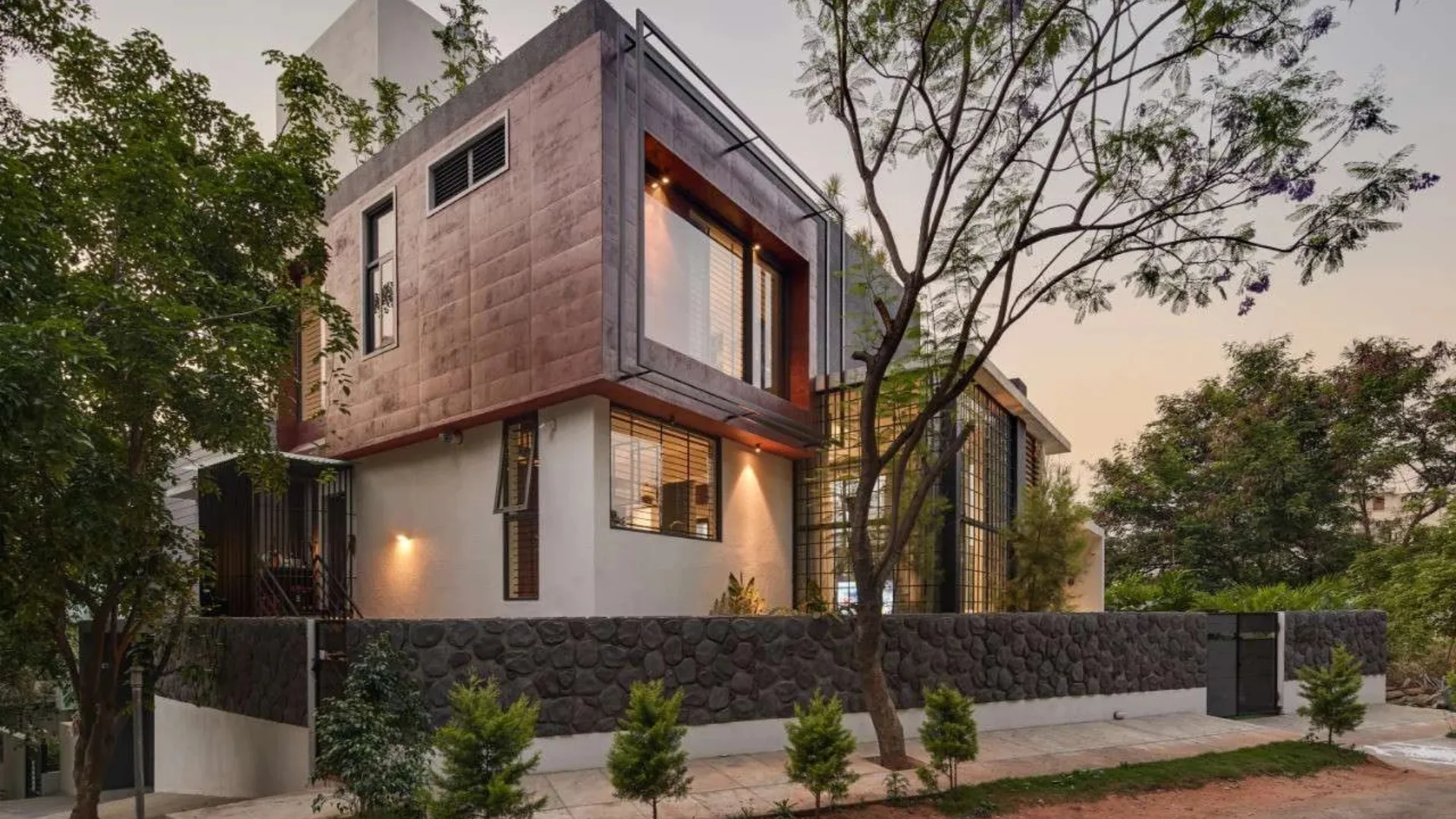 Modern multi-story home featuring a copper-clad cantilevered box and stone compound wall designed by architects in Bangalore